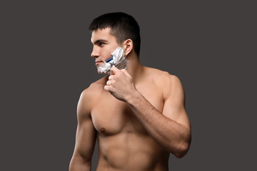 Handsome young man shaving against grey background