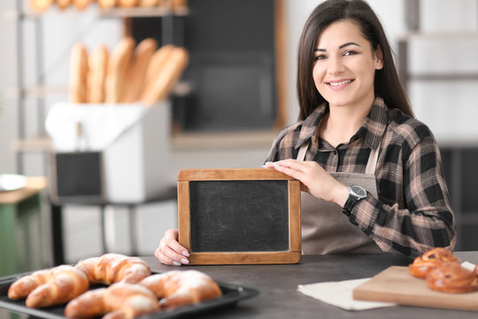 Portrait of young woman with mini chalkboard in bakery. Small business owner