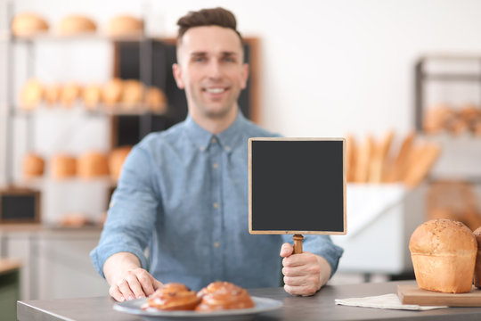 Portrait of young man with mini chalkboard in bakery. Small business owner