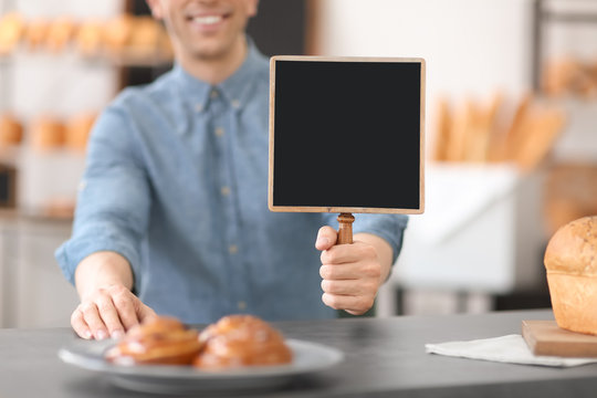 Man holding mini chalkboard in bakery. Small business owner