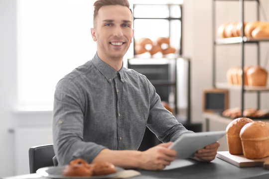 Young man using tablet computer in bakery. Small business owner
