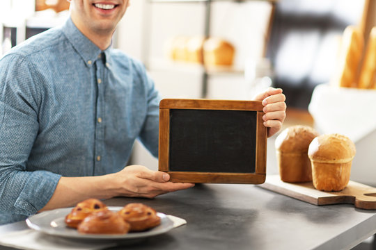 Man holding mini chalkboard in bakery. Small business owner