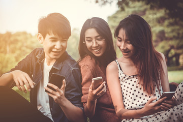 Group of teenage asian friend having fun together with using mobile phone in park