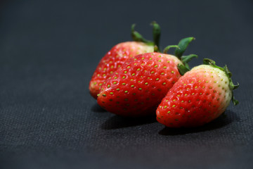 Three Strawberry on the black floor. it is a sweet soft red fruit with a seed studded surface.