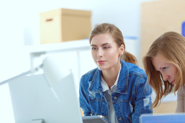 Two young woman standing near desk with instruments, plan and laptop.