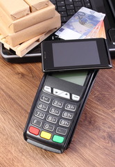 Credit card reader with mobile phone with NFC technology, currencies euro, laptop and wrapped boxes on wooden pallet