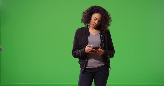 Cool woman in black bomber jacket receiving text message on smart phone on greenscreen. Millennial using cellphone messaging app on green screen for compositing or keying. 4k