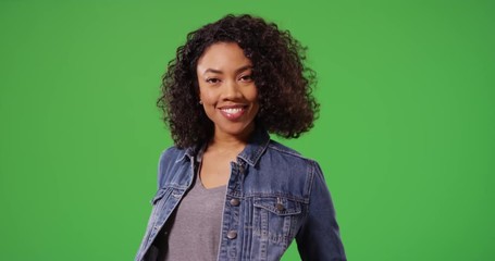 Portrait of happy black woman in jean jacket posing playfully on green screen. Close up of stylish African American Millennial girl smiling and laughing on greenscreen for keying or compositing. 4k - Powered by Adobe