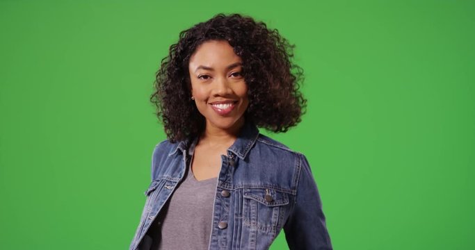 Portrait of happy black woman in jean jacket posing playfully on green screen. Close up of stylish African American Millennial girl smiling and laughing on greenscreen for keying or compositing. 4k
