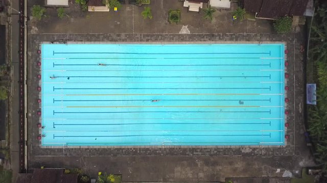 Aerial View from Above on Public Open Water Swimming pool. Sportive People Practice and Relax in Big Swimmingpool. 4K. Bali, Indonesia.
