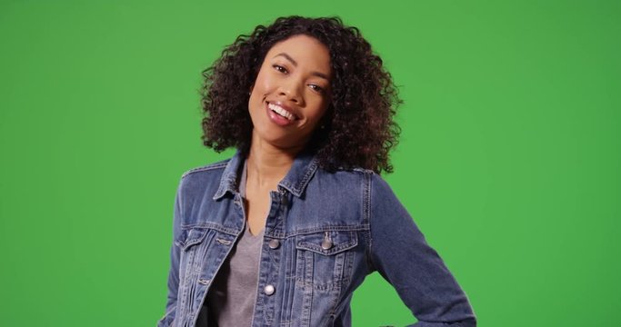 Portrait of laughing black woman in jean jacket posing playfully on greenscreen. Close up of stylish African American Millennial girl smiling and posing on green screen for keying or compositing. 4k