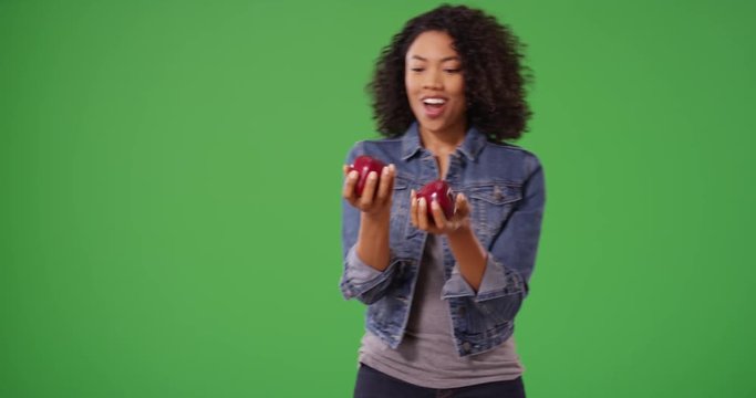 Playful cute black woman juggling apples on greenscreen background and laughing. Happy smiling African American girl juggles fruit on green screen for keying or compositing. 4k
