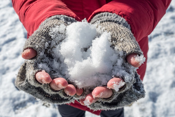 hands with gloves holding snow on a red dress in a sunny winter morning