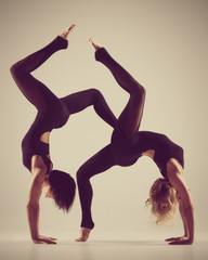 Flexible women exercising. Beautiful flexible woman doing partner yoga on grey background. image with vintage toning