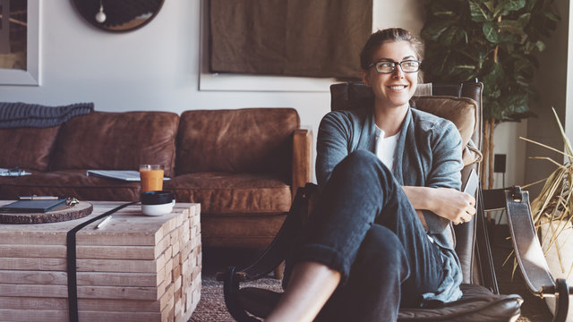 Portrait of smiling woman with mobile phone sitting in cozy loft studio