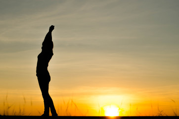 Woman silhouette is standing, raise one's hand for exercise, on evening .