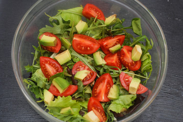 Top View of Fresh Salad with Avocado, Tomatoes and Tuna and ruccola Leaves. Healthy, diet and Fitness Food concept. Black board.