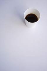 Paper (disposable) white cup with coffee close-up. Blurred background. Top view with copy space