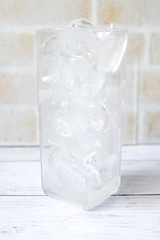 Transparent glass fill with ice cube on white wooden background.