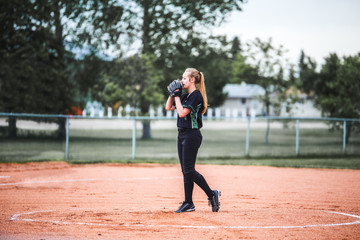 A teenage girl holding glove up to her face with long hair in a ponytail standing on the pitchers...