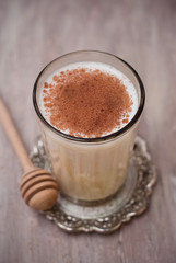 Glass of Milk with Cinnamon or Cocoa Powder with Honney Spoon on rustic background. Healthy Breakfast. Vertical Image.