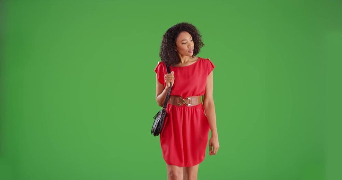 Stylish black woman in red dress with purse walking toward camera on green screen background. Fashionable African American woman walks while laughing and smiling for greenscreen compositing. 4k