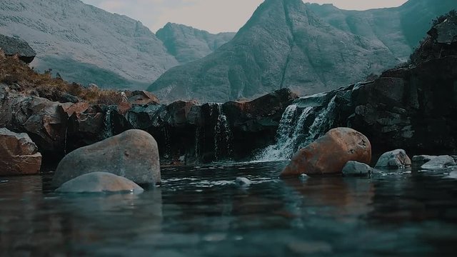 Crystal Clear Water at River with Waterfalls and Looming Mountains