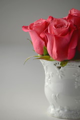 A bunch of pink roses in a white vase on a solid pastel color background with copy space.