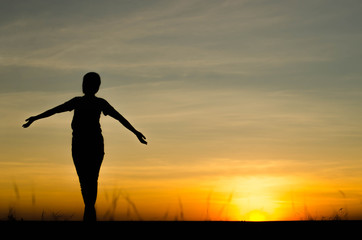 Woman silhouette is standing, raise one's hand for exercise, on evening .