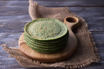 Wooden board with a stack of spinach pancakes on the wooden table, rustic style, selective focus © olepeshkina
