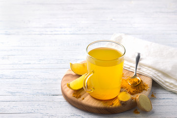 Energy tonic drink with turmeric, ginger, lemon and honey on a wooden board, free space, selective focus