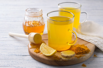 Energy tonic drink with turmeric, ginger, lemon and honey on a wooden board, selective focus