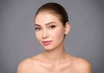 Portrait of beautiful young woman with clear skin on grey background