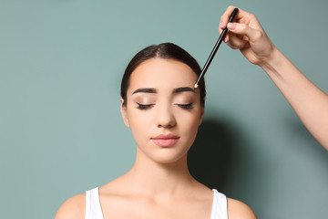 Young woman undergoing eyebrow correction procedure on color background