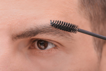 Young man correcting shape of eyebrows, closeup