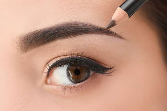 Young woman correcting shape of eyebrows, closeup
