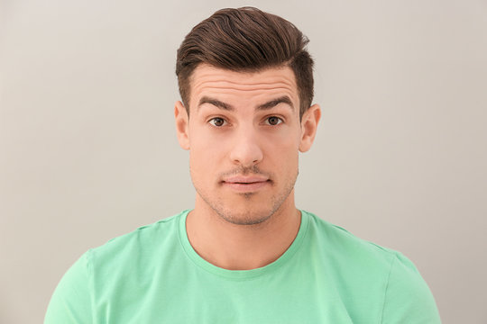 Young man with raised eyebrows on light background