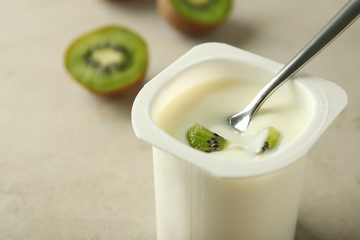 Plastic cup with yummy kiwi yogurt and spoon on table, closeup