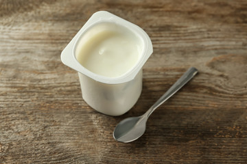 Plastic cup with yummy vanilla yogurt on wooden table