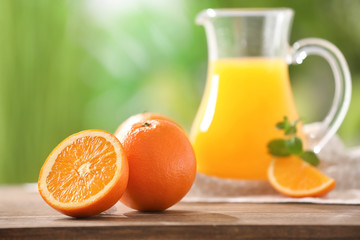 Ripe oranges and pitcher with juice on table