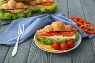 Plate with tasty croissant sandwich on table