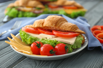 Plate with tasty croissant sandwich on table