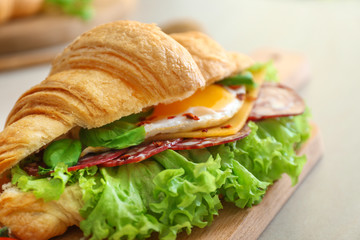 Wooden board with tasty croissant sandwich on table