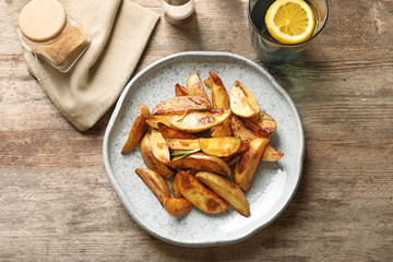 Plate with tasty potato wedges on table