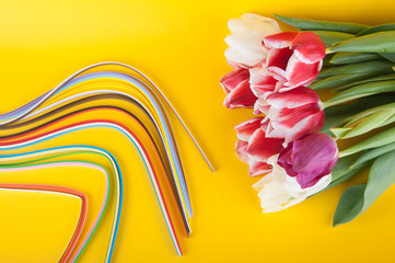 Top view on fresh spring bouquet and multicolored paper strips on yellow background