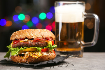 Tasty burger on slate plate against dark background