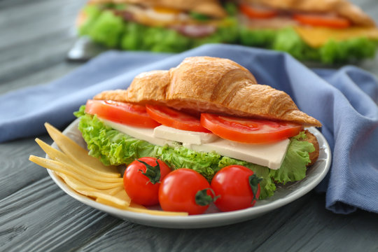 Plate with tasty croissant sandwich on table