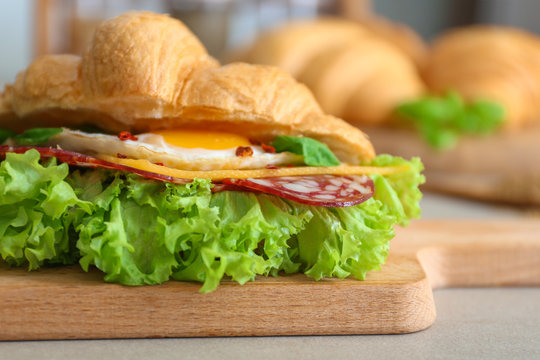 Wooden board with tasty croissant sandwich on table