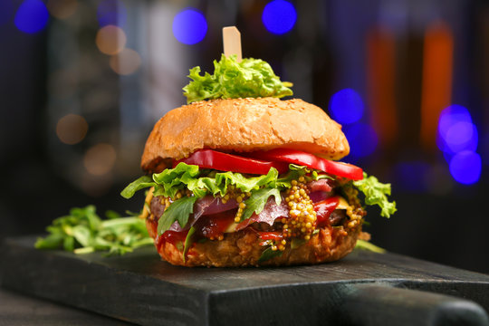 Tasty burger on wooden board against dark background