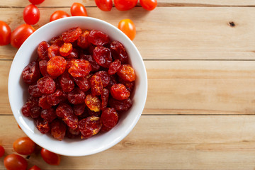 dried cherry tomatoes in white bowl on wooden background.